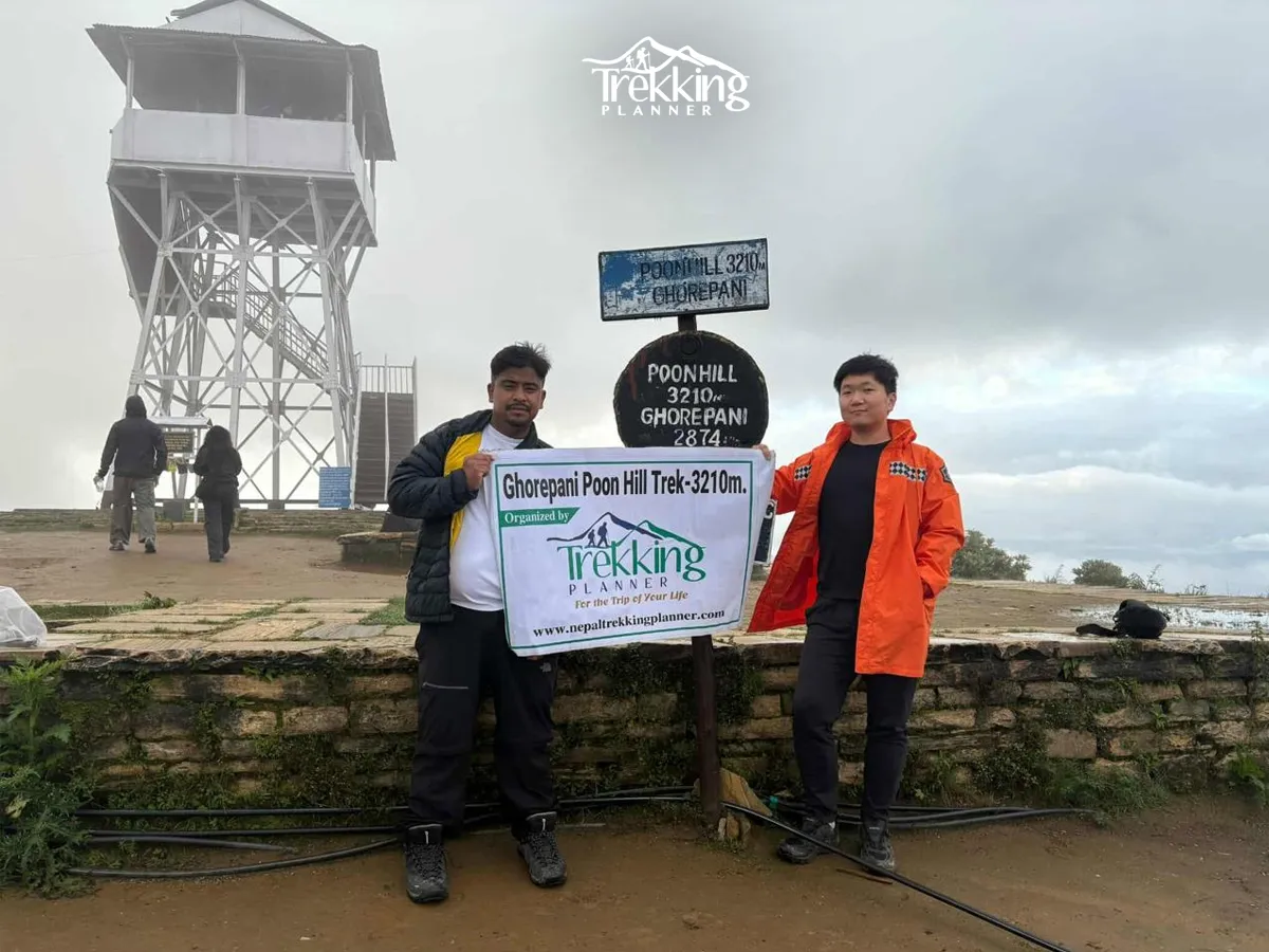 Trekkers at the Ghorepani Poon Hill Trek viewpoint standing beside the 3210m sign with Trekking Planner banner in Nepal