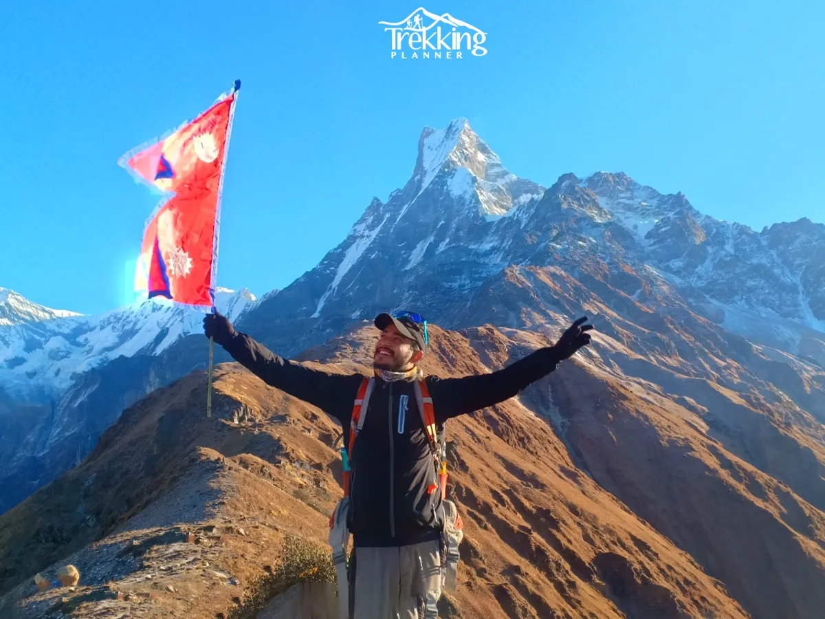 Trekker holding the Nepal flag at Mardi Himal Base Camp during the Mardi Himal Base Camp Short Trek with Machhapuchhre behind.