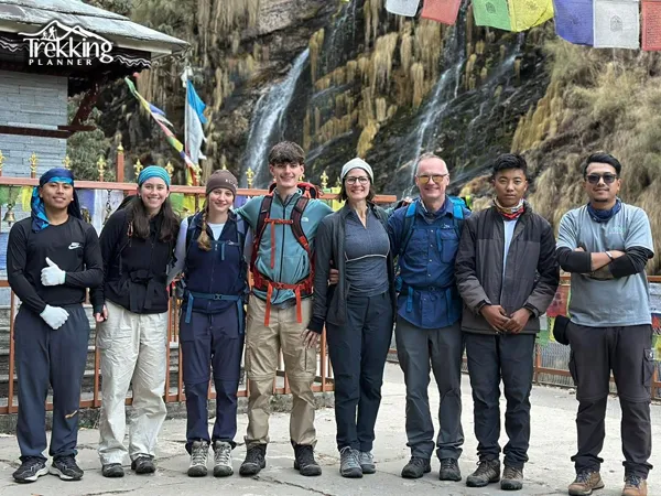 Family trekking group with local guides near a scenic waterfall in the Annapurna region of Nepal