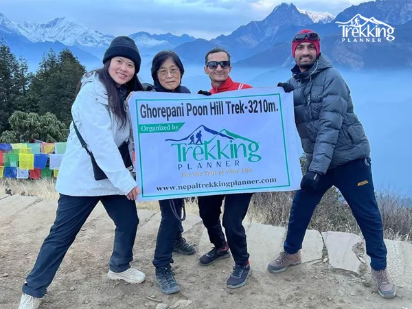 Trekkers posing with Trekking Planner banner at Poon Hill viewpoint during the Ghorepani Poon Hill Trek with Annapurna mountains in the background