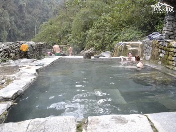 Trekkers resting near natural hot springs along the Annapurna trekking route surrounded by Himalayan mountains